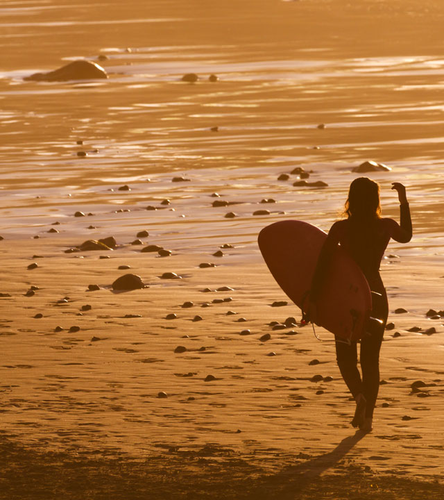 Chica camina por la orilla de la playa con su tabla de surf bajo el brazo